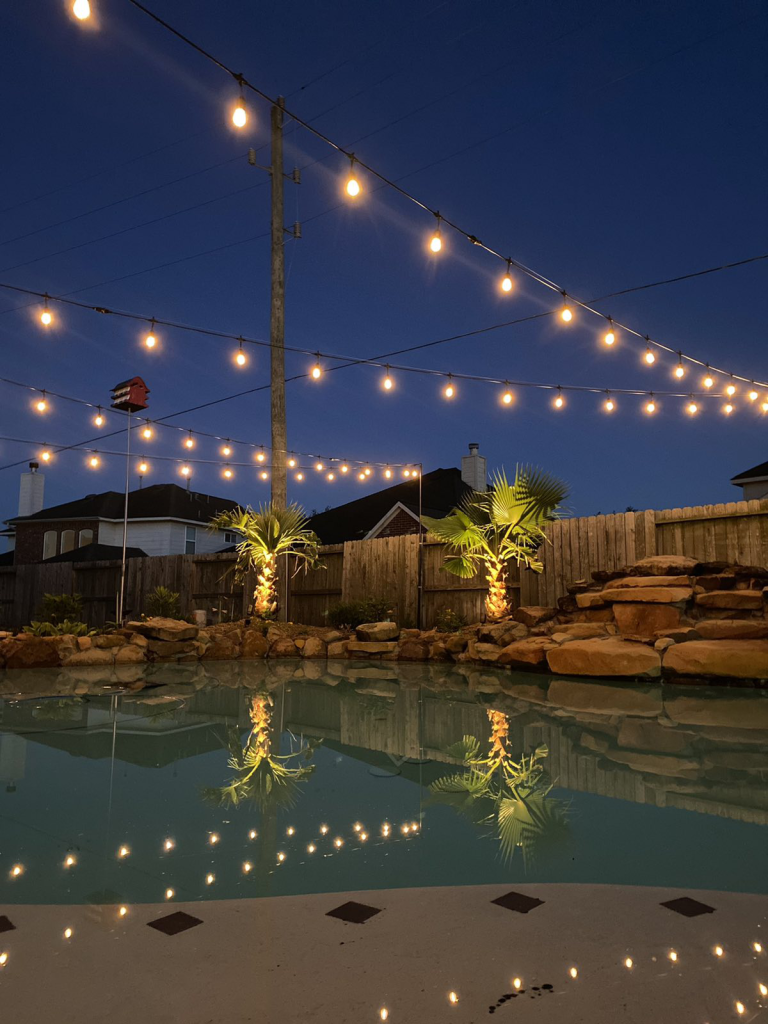 A backyard with a pool illuminated for a party.